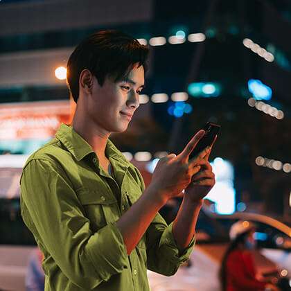 Guy in green uses mobile on dark lit city street