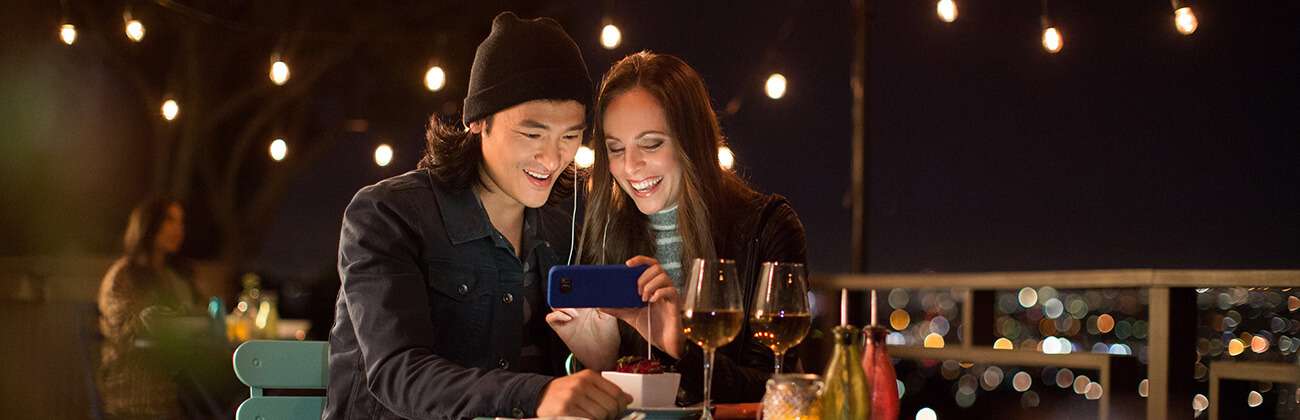 Traveling couple look at phone together in an outdoor bistro at night